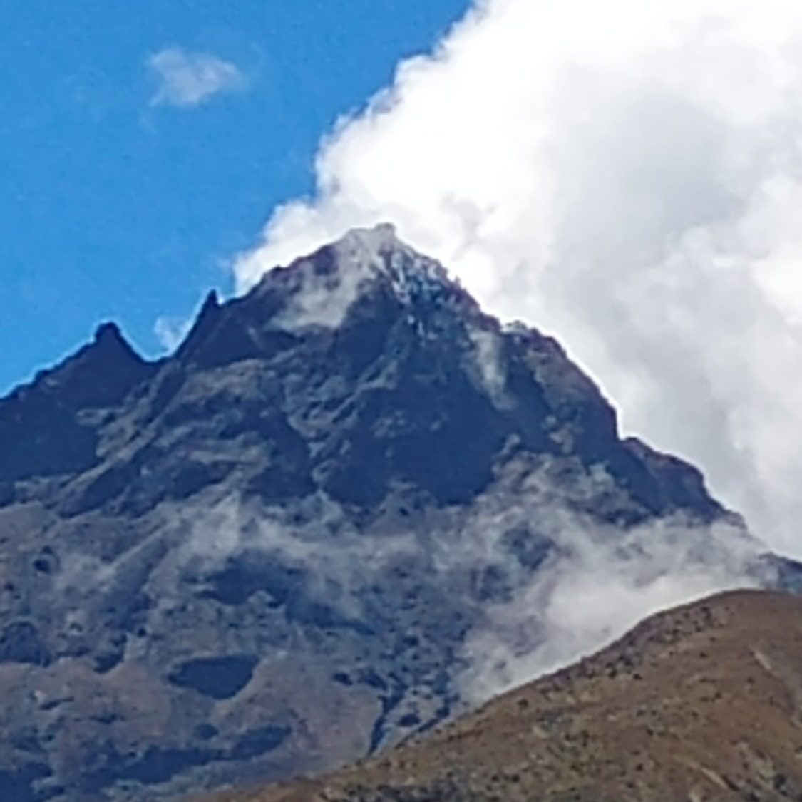 Ecuador Spitze eines hochaufragenden Berges mit Wolken im Hintergrund.